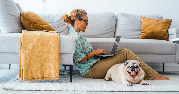 women sitting on the floor working on her laptop with her dog sitting with her