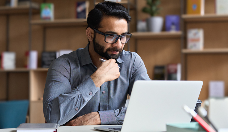 smiling indian business man working on laptop at home office