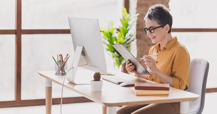 women sitting at desk reviewing papers on clipboard