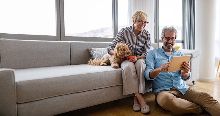 Couple sitting on a couch with their dog, looking at an tablet